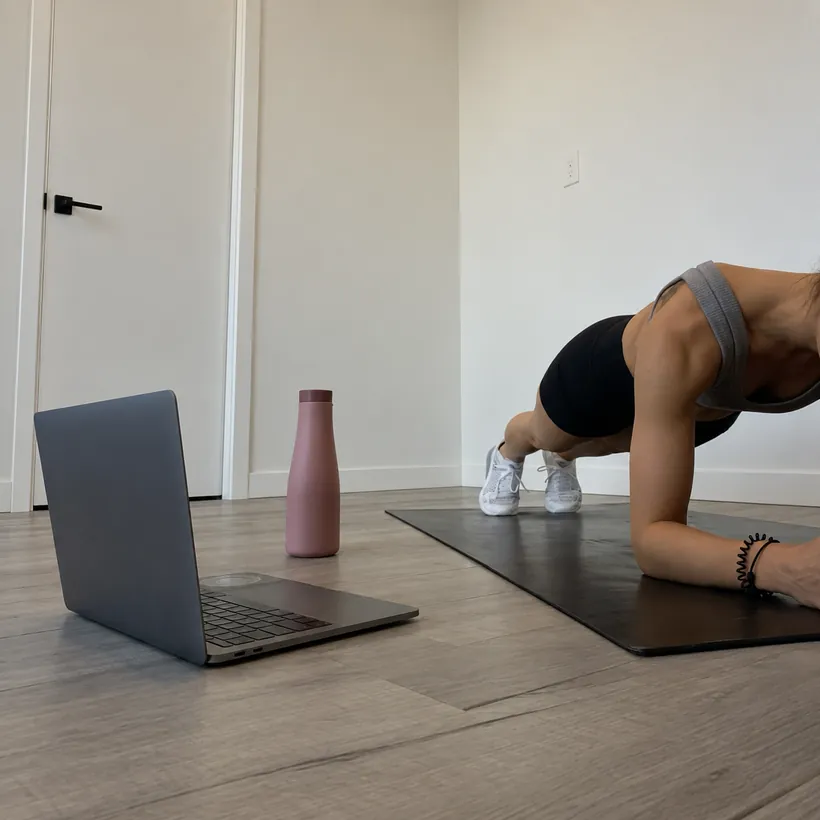 Mulher treinando em casa sobre o tapete, acompanhando uma aula no notebook