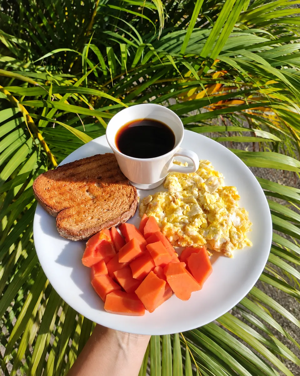 Café da manhã completo — ovos, torrada, mamão e café — na luz da manhã